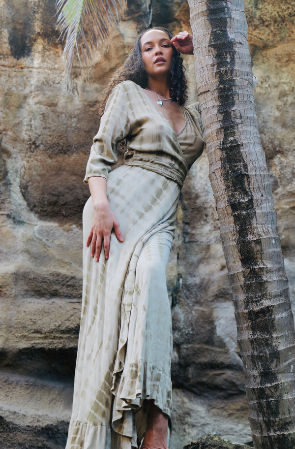 Model wearing LOLA khaki wrap dress leaning against a palm tree