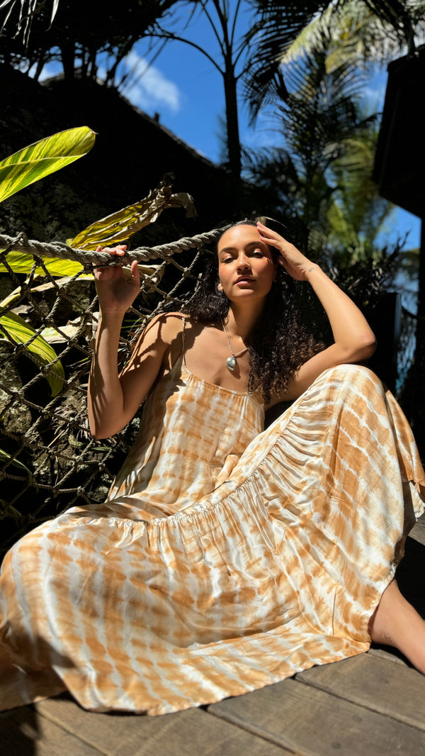 Model wearing ARIE orange tie-dye dress on a Caribbean beach