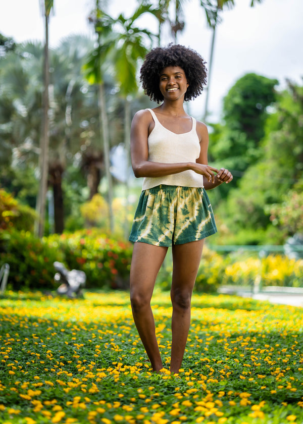 Front view of BLISS green and yellow tie-dye shorts in a Caribbean garden