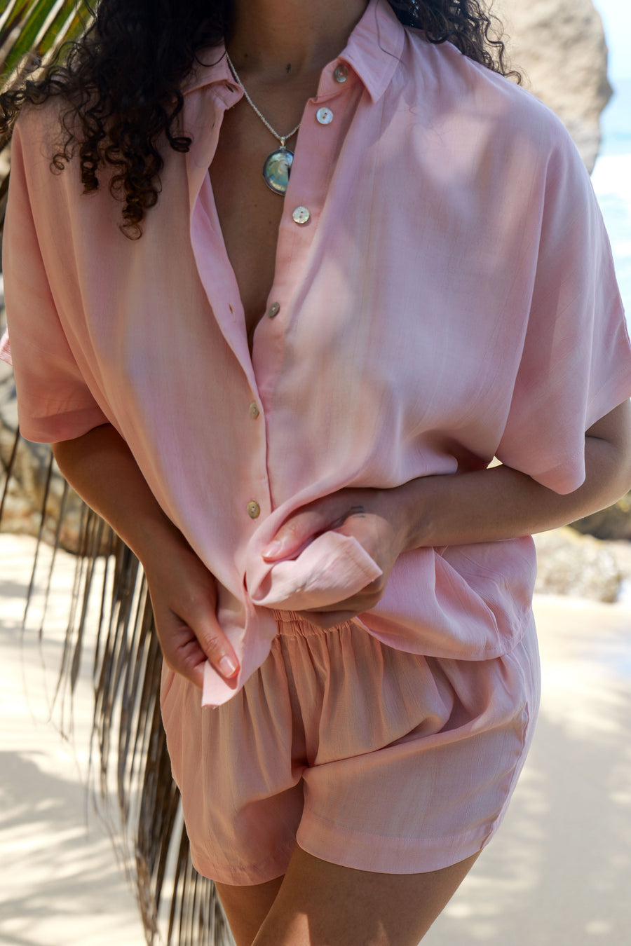 AURA pink tie-dye shirt worn open over a bikini beside the rocks