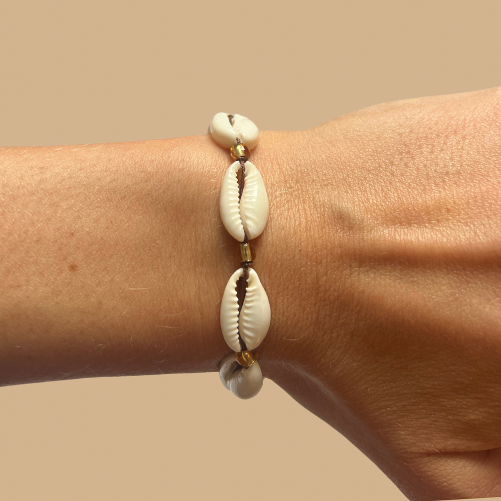 Corrie shell bracelet with gold details worn on a wrist on the beach
