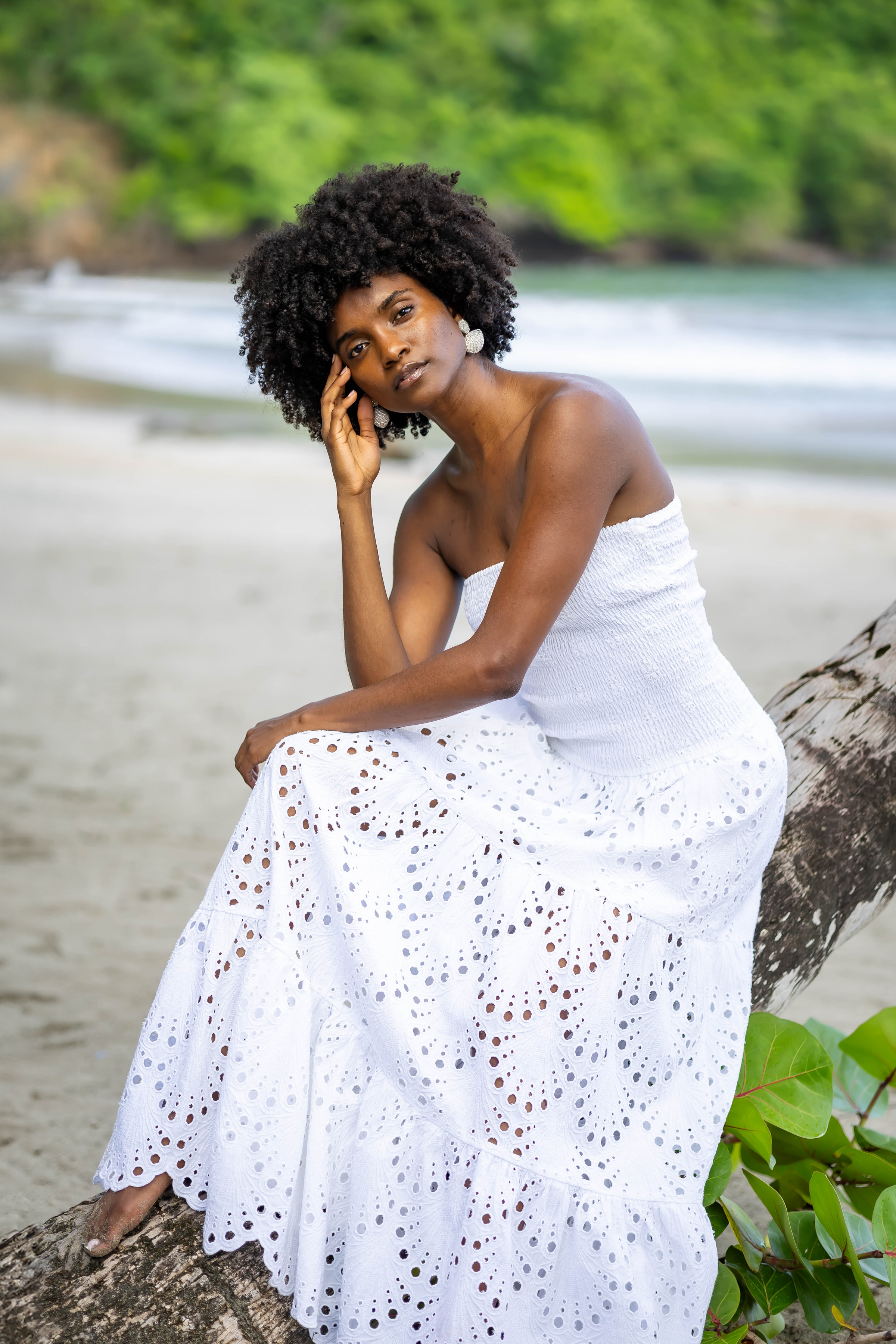 Model sitzt im weißen bestickten PERLA Baumwollkleid auf Treibholz