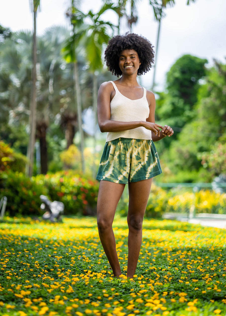Front view of BLISS green and yellow tie-dye shorts in a Caribbean garden